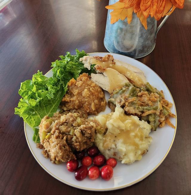 A holiday plate of roasted turkey with gravy, mashed potatoes, cornbread dressing, green bean casserole, sweet potato soufflé and fresh cranberries