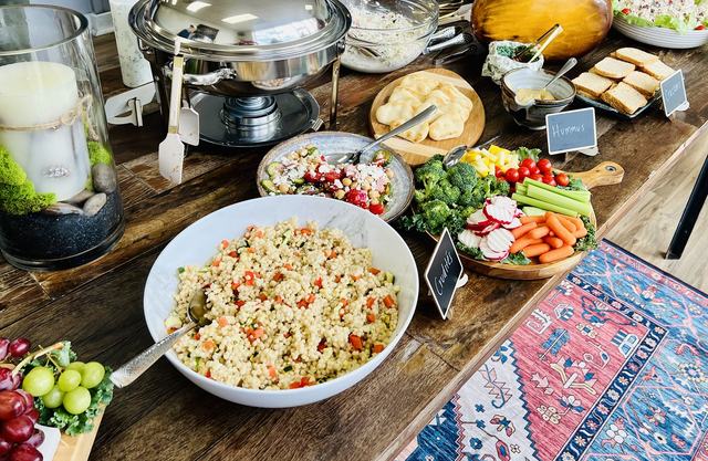 A party spread with pearl couscous salad, chickpea salad, crudités, pita and hummus